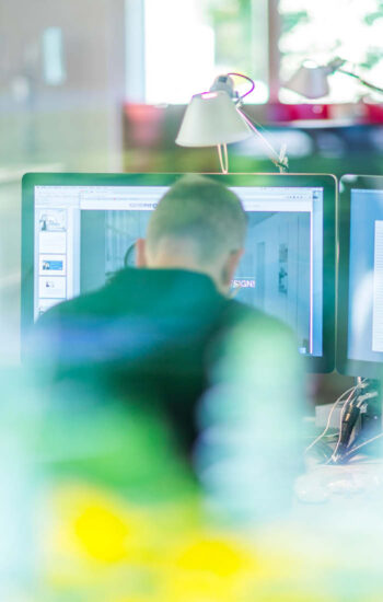 Mitarbeiter arbeitet am Computer mit mehreren Bildschirmen im Büro und zeigt digitale Gestaltung und Designprozess